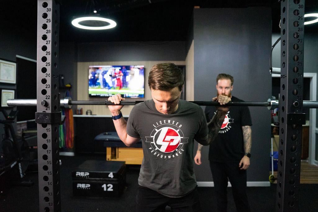 Athlete setting up for a back squat at Licensed Performance in Cary, NC, with Dr. Casey Irvine spotting in the background.